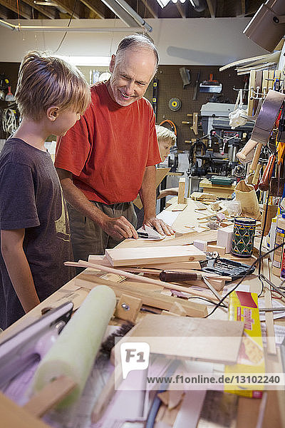 Smiling senior man looking at grandson while working in workshop