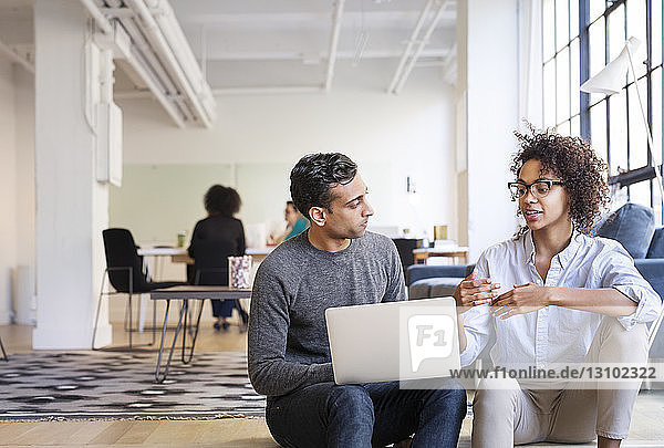 Geschäftsleute  die sich unterhalten  während sie einen Laptop im Büro benutzen