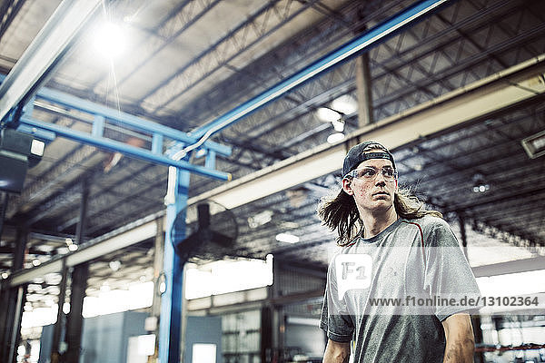 Worker looking away while standing in steel factory