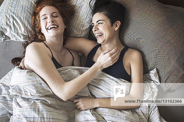 High angle view of cheerful lesbians relaxing on bed
