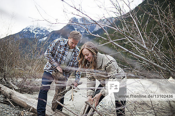 Young couple collecting wood for campfire against mountains