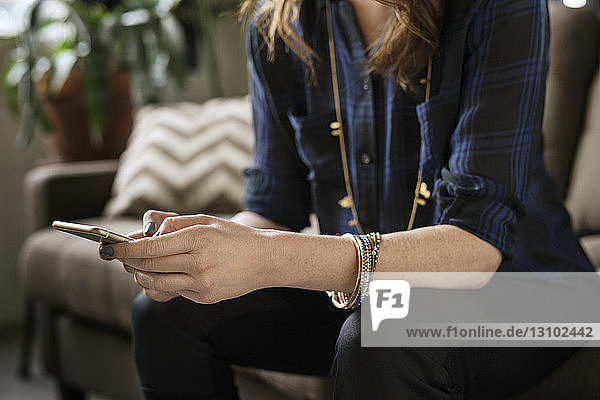 Midsection woman using smart phone while sitting on sofa