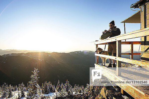 Mann steht im Winter mit Hund auf dem Balkon eines Fremdenverkehrsortes