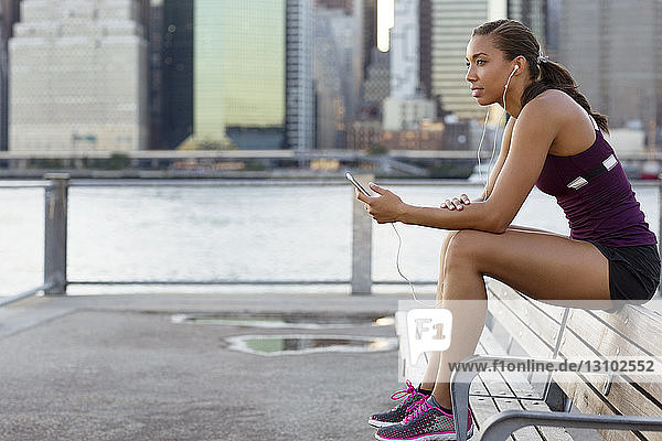 Sportler hört Musik  während er auf einer Bank am Fluss sitzt