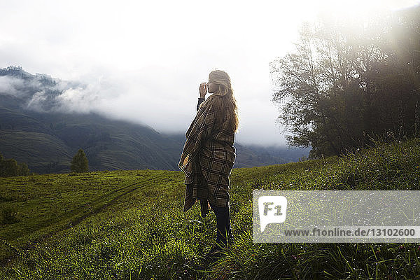 Full length of woman wrapped in blanket standing on grassy field during foggy weather