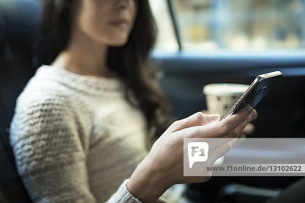 Mitschnitt einer Frau  die ein Smartphone benutzt  während sie im Taxi Einwegglas hält