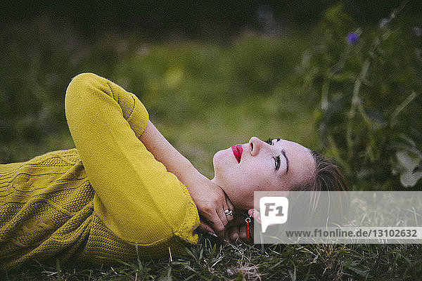 Seitenansicht einer nachdenklichen jungen Frau  die auf einem Grasfeld liegt