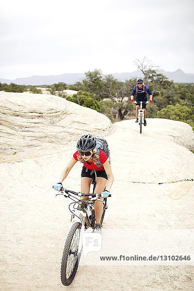 Couple riding bicycles on rocks against clear sky