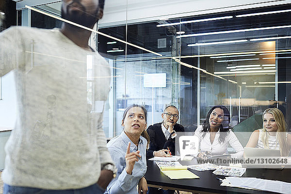 Multi-ethnische Kollegen betrachten Unternehmer bei einer Präsentation in einer Sitzung im Sitzungssaal