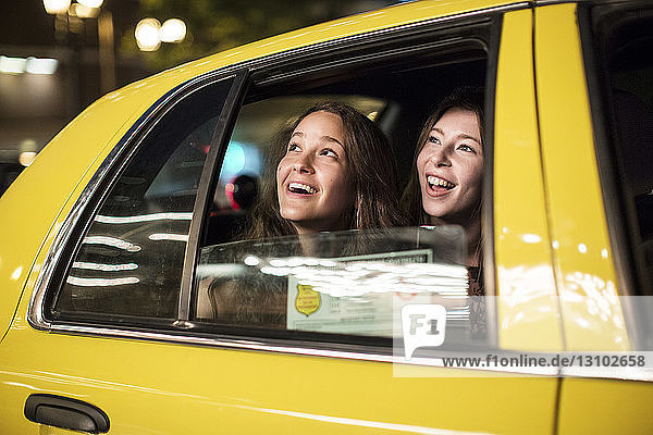 Lächelnde Freundinnen  die während einer Taxifahrt durchs Fenster schauen