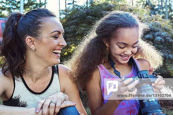 Glückliche Mutter und Tochter schauen auf eine Digitalkamera  während sie im Hof sitzen