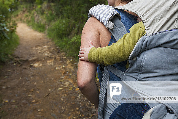 Rear view of mother carrying son in baby carriage while walking in forest