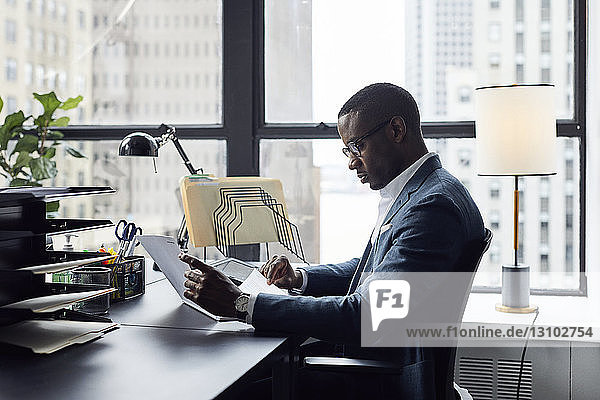 Serious businessman working while sitting against window in office