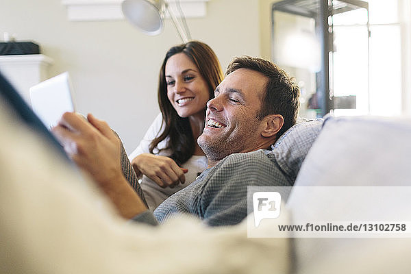 Glückliches Paar benutzt digitales Tablet während es sich zu Hause auf dem Sofa entspannt
