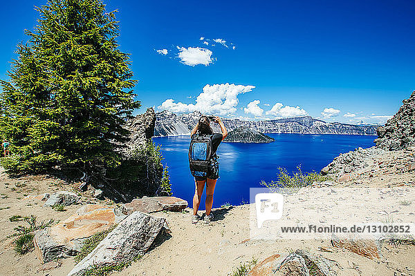 Rear view of female hiker with backpack photographing while standing against Crater Lake