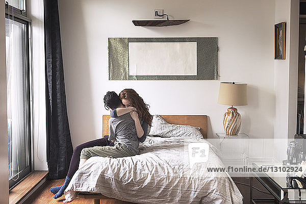 Lesben umarmen sich  während sie zu Hause auf dem Bett sitzen