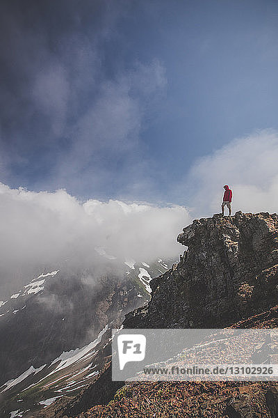 Side view of man standing on cliff against cloudy sky