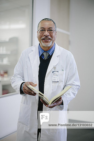 Portrait of smiling male doctor with book standing in hospital