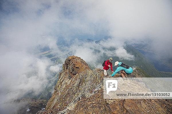 Hochwinkelaufnahme eines Wanderers  der einem Freund auf einem Berg inmitten von Wolken hilft