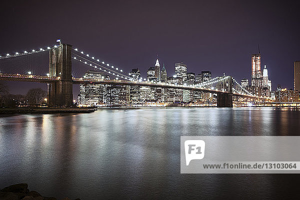 Beleuchtete Brooklyn Bridge über den East River mit der Stadt im nächtlichen Hintergrund