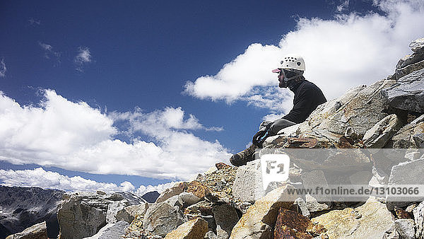 Seitenansicht eines auf einem Felsen sitzenden Mannes gegen den Himmel