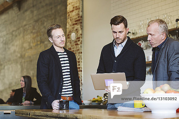 Geschäftsmann benutzt Laptop-Computer  während er mit männlichen Kollegen im Büro steht