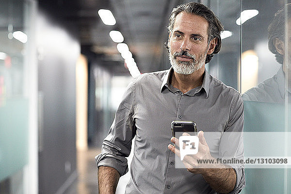 Geschäftsmann schaut weg  während er ein Smartphone in der Büro-Lobby hält