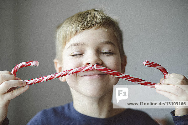 Verspielter Junge  der sich zu Hause mit Zuckerstangen einen Schnurrbart macht
