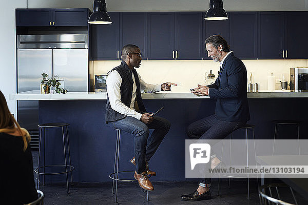 Männliche Kollegen unterhalten sich  während sie auf Hockern an der Küchentheke im Kreativbüro sitzen