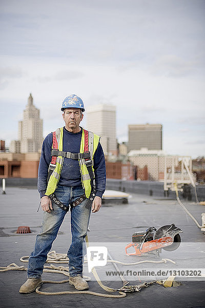 Porträt eines männlichen Arbeiters  der auf einem Gebäude auf einer Baustelle vor bewölktem Himmel steht