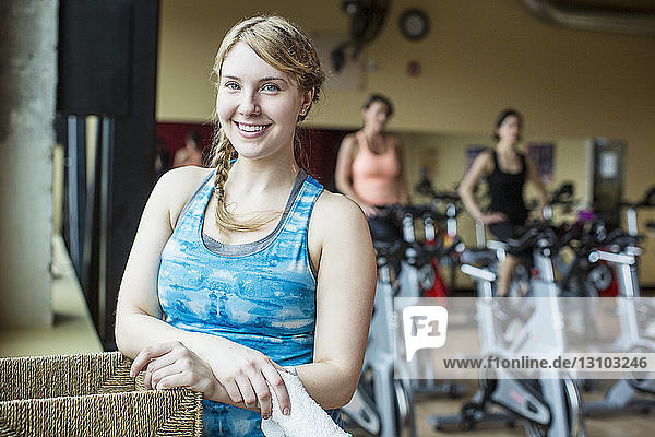 Porträt einer lächelnden Frau mit Freunden  die im Hintergrund im Fitnessstudio trainieren