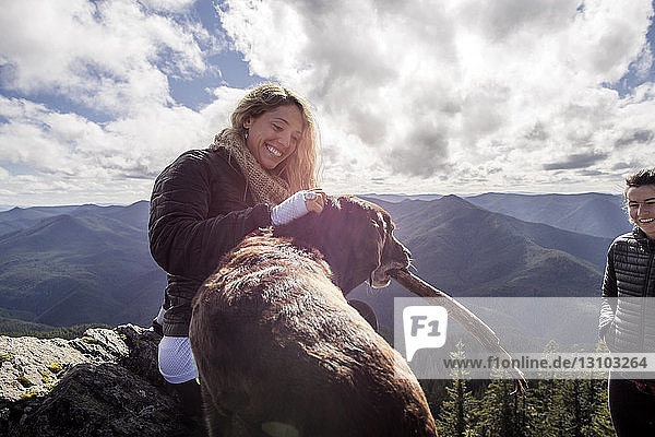 Woman playing with dog at mountain cliff against cloudy sky