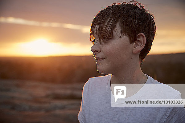 Junge schaut weg  während er bei Sonnenuntergang auf dem Berg Arabien vor bewölktem Himmel steht