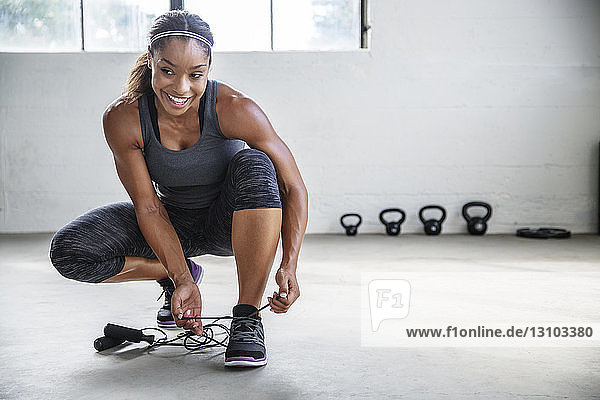 Smiling female athlete tying shoelace in gym