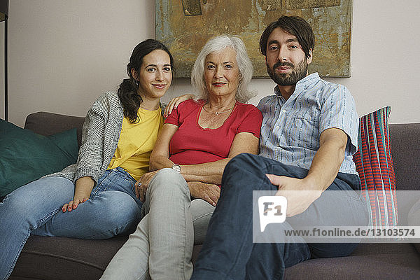 Portrait senior mother sitting with daughter and son on living room sofa