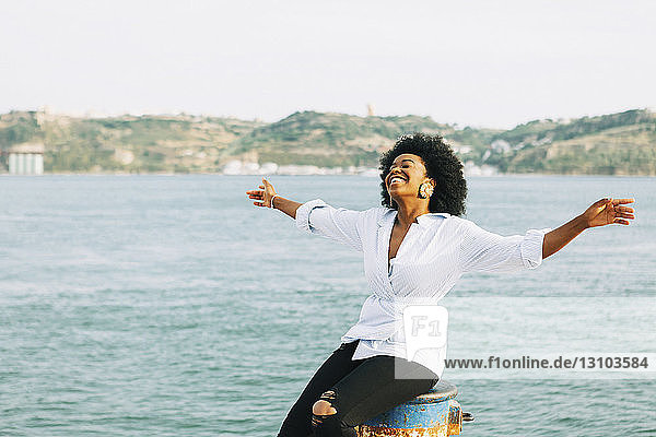 Carefree young woman with arms outstretched at waterfront  Belem  Lisbon  Portugal