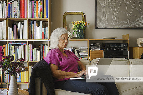 Senior woman using laptop on living room sofa