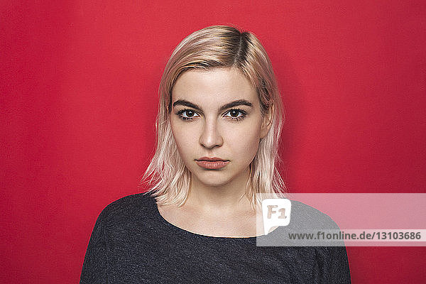 Portrait of woman with bleached hair and serious expression against red background