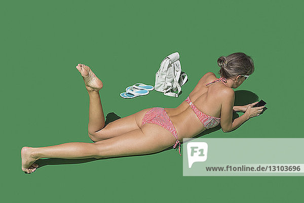 Woman in bikini sunbathing on green background