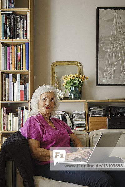 Portrait confident senior woman using laptop on living room sofa