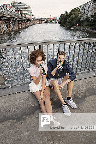 Junges Paar trinkt Bier auf einer städtischen Brücke über einen Fluss