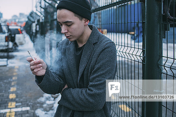 Junger Mann raucht am Winterzaun