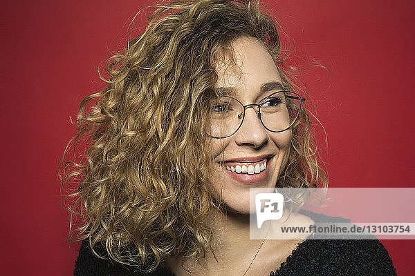Portrait of woman smiling with curly hair and wearing glasses against red background