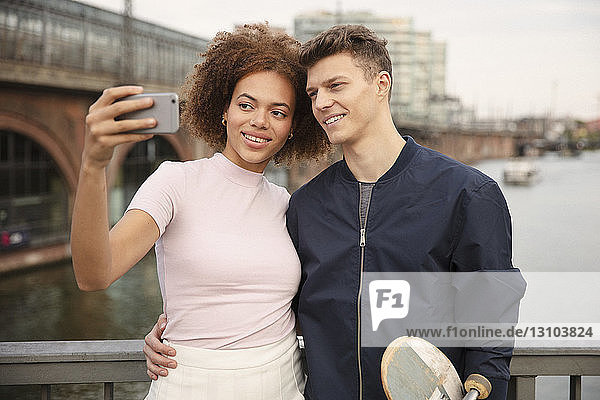 Junges Paar mit Smartphone nimmt Selfie auf Brücke