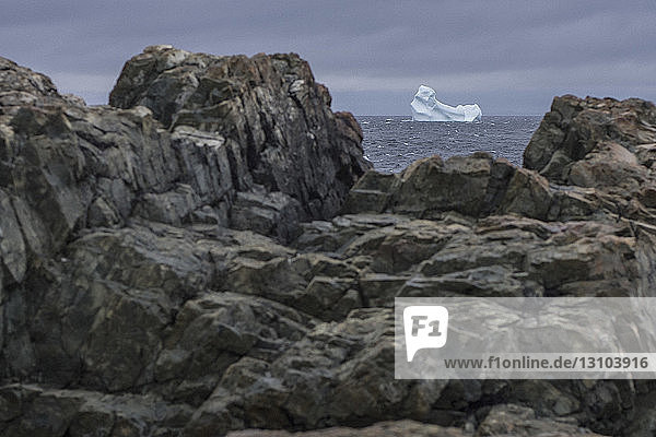 View of iceberg in sea through rocks on shore  Fogo Island  Newfoundland  Canada