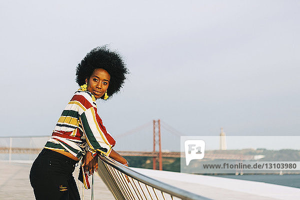 Portrait confident young woman at waterfront with 25 de Abril Bridge in background  Lisbon  Portugal