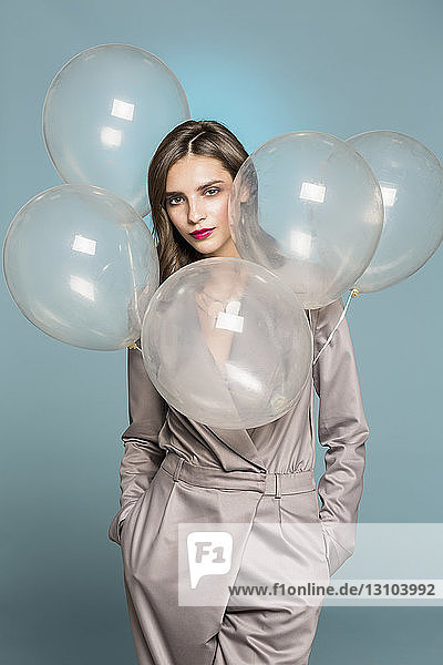 Portrait of female fashion model standing with balloons against blue background