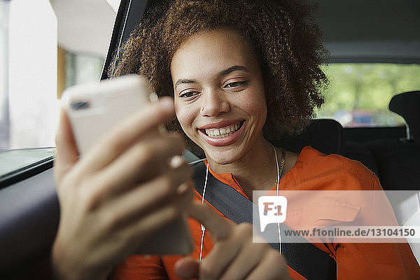 Lächelnde junge Frau  die ein Smartphone im Auto benutzt