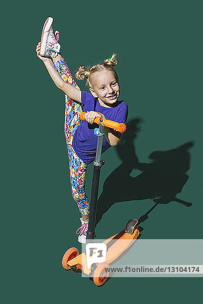 Playful girl with scooter doing standing splits on green background