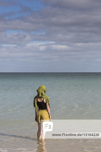 Gelassene Frau mit Kopftuch watet im sonnigen Meer